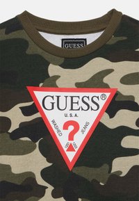 Kameramønstret bomulls T-skjorte med en rød trekantlogo med "GUESS U.S.A." og teksten "WASHED JEANS" i sentrum, rund krage.