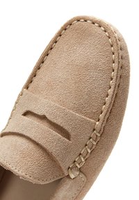 Gros plan de la partie avant d'une chaussure en daim beige avec des coutures détaillées et une fente sur la bande supérieure.
