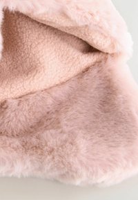 Tissu en fausse fourrure rose pâle, doux, avec une texture dense et pelucheuse. Une doublure intérieure lisse complète l'extérieur cosy. Aucun matériel visible.