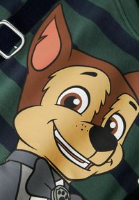 Grønt og marineblått stripet stoff med et karakters ansikt med brune ører, gul snute og sløyfe, trykt i tegneseriestil.