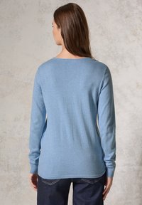 Ljusblå långärmad tröja med rundad halsringning, mjuk textur och åtsittande ärmslut, i kombination med mörkblå jeans.