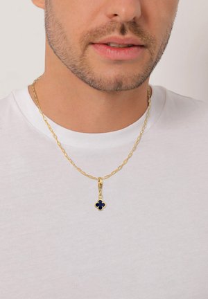 Mand iført hvid t-shirt og guldkæde med en lille blå firkløver vedhæng, close-up af nederste del af ansigtet og halsen.