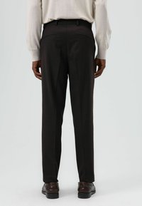 Donkerbruine, op maat gemaakte broek met een gladde textuur, voorzien van een smalle pasvorm, twee achterzakken en een formeel ontwerp. Draagt een licht beige overhemd.