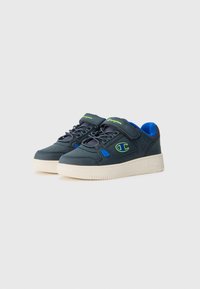 Zapatillas con una parte superior azul oscura, acentos verdes y suela de goma blanca. Incluyen cordones y una correa de Velcro para el ajuste.