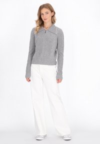 Grijze gebreide cardigan met een textuurpatroon, volle rits, grote kraag en ribgebreide manchetten, gecombineerd met witte broek met brede pijpen en sneakers.