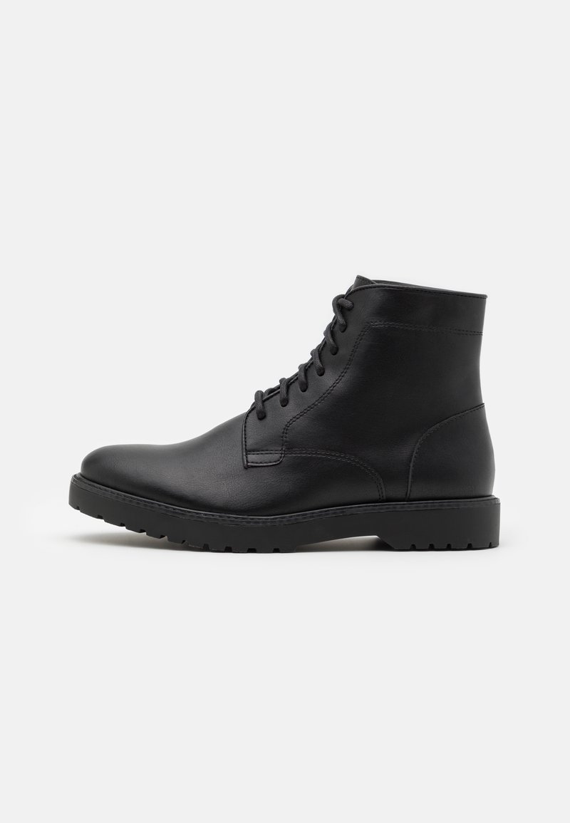 Bottine en cuir noir avec fermeture à lacets à l'avant, détails cousus et semelle en caoutchouc robuste sur un fond clair uni.