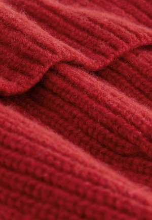 Röd stickad tyg med texturerad ribbing. Mjuk, fluffig yta med överlappande veck som visar djup och värme.