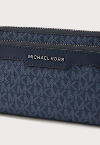 Πορτοφόλι από δέρμα σε ναυτικό μπλε χρώμα με υφή που επαναλαμβάνει το λογότυπο και αξεσουάρ σε ασημί απόχρωση. Κλείνει με φερμουάρ στην κορυφή.