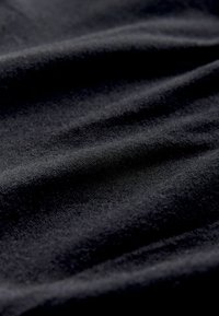 Melnā audumā ir gluda, nedaudz teksturēta virsma, ar plānām krokām un grumbām. Materiāls izskatās mīksts un viegls.