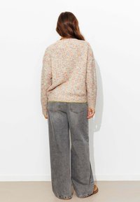 Pull multicolore tricoté avec une coupe décontractée, doté d'un col rond et d'un ourlet côtelé. Associé à un jean gris à jambes larges.