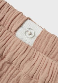 Tissu rose texturé avec des détails froncés, présentant un bandeau élastique blanc et un bouton transparent. Gros plan sur la construction de la taille.