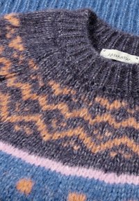 Pull en laine tricoté avec une base gris foncé, présentant des motifs en zigzag orange et des rayures horizontales rose clair et bleues. Étiquette visible.