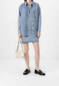 Denim shirt and skirt set in light blue. Shirt has buttons and pocket; skirt features frayed hem. Paired with black loafers and beige socks.