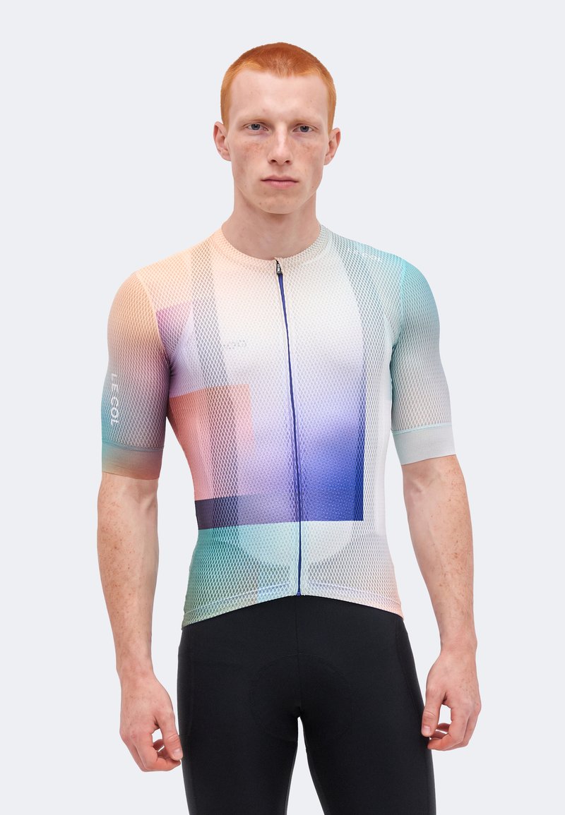 Mann mit kurzen roten Haaren, der ein eng anliegendes, mehrfarbiges Netz-Radtrikot und schwarze Radhosen trägt, blickt nach vorne vor weißem Hintergrund.