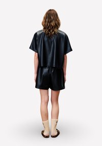 Kortärmelig crop top van zwart namaakleer gecombineerd met bijpassende zwarte shorts, met een relaxte pasvorm en een gladde textuur. Geaccentueerd met beige sokken en slides.