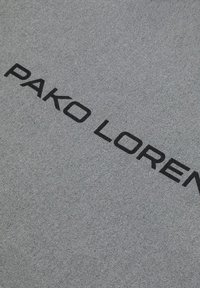 Szary materiał z wyraźnym czarnym napisem "PAKO LOREN". Tkanina ma subtelną teksturę z drobnym splotem.