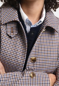 Brun og blå ternet frakke med krave, der har store knapper, en lomme med klap, og lagdelt med en marineblå sweater og en lyseblå skjorte.