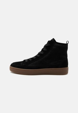 Μαύρο sneaker ψηλού τύπου με υφή σουέτ, μαύρα κορδόνια και καφέ λαστιχένια σόλα σε απλό λευκό φόντο.