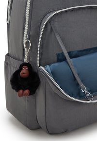 Zaino in tessuto grigio con un portachiavi a forma di gorilla nero in peluche, zip argentate e una tasca laterale con un inserto blu.