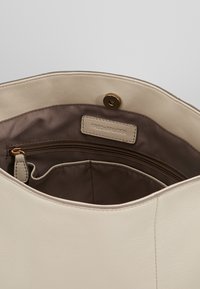 Beige läderhandväska inredning med en central dragkedjeficka, slät textur, subtil branding och en tryckknappsstängning.