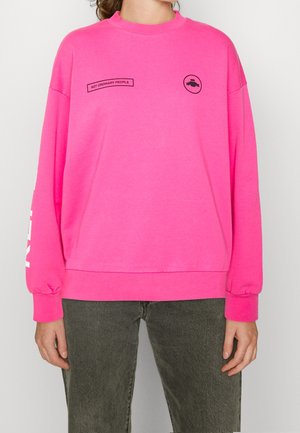 Ljusröd sweatshirt med rund hals, sänkta axlar och långa ärmar. Har svart text och en cirkulär grafik på bröstet.