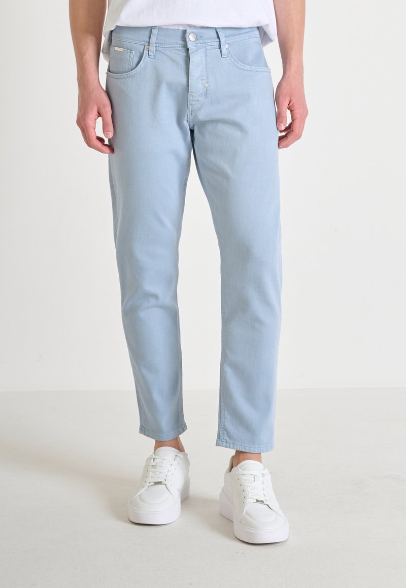 Jeans in denim blu chiaro con una vestibilità a gamba dritta, caratterizzati da cinque tasche e cuciture sottili. Abbinati a sneakers bianche.