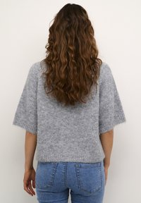 Grey short-sleeve sweater made of soft, fuzzy material, featuring a loose fit and a cropped design, paired with blue denim jeans.