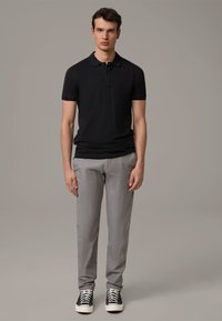 Schwarzes Polohemd mit kurzen Ärmeln, graue Hose und schwarze Turnschuhe mit weißen Schnürsenkeln. Einfaches Design, figurbetonte Silhouette und glatte Stofftextur.