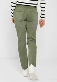Pantalon chino vert olive à coupe droite, avec deux poches arrière et des détails de couture subtils, assorti à des baskets blanches montantes.