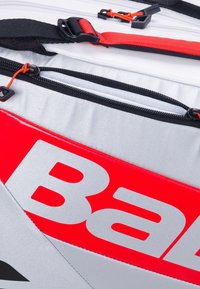 Zaino sportivo rosso e argento con zip, spallacci neri e un grande logo. Il materiale è resistente e con una superficie liscia.
