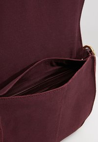 Borsa in suede marrone con chiusura a patta, tasca interna e rivestimento liscio. Caratterizzata da dettagli in metallo dorato.