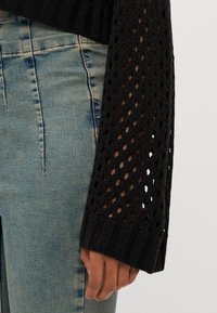Maglione nero lavorato a maglia con motivo a trama aperta e texturizzato sulle maniche, abbinato a jeans di denim azzurro chiaro a vita alta.