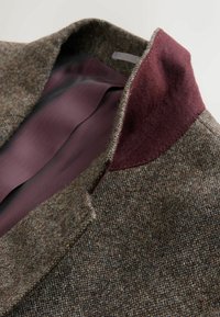 Brown tweed blazer with a textured finish, featuring a burgundy felt collar and a smooth, patterned inner lining in mauve.