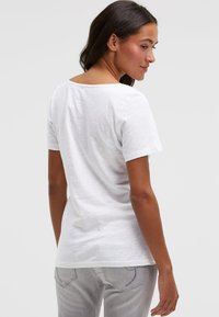 Weißes Kurzarm-T-Shirt mit rundem Halsausschnitt, lockerem Schnitt und weicher Textur. Rückansicht zeigt leicht abfallenden Saum und glattes Gewebe.