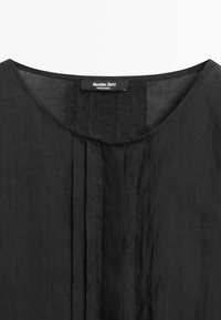 Close-up of a black garment neckline with vertical pleats and a sewn-in label reading Massimo Dutti, made in India.