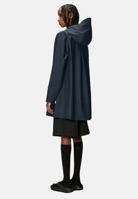 Giacca impermeabile blu navale con cappuccio, maniche lunghe e taglio dritto, abbinata a pantaloni corti fino al ginocchio e calze alte fino al ginocchio.