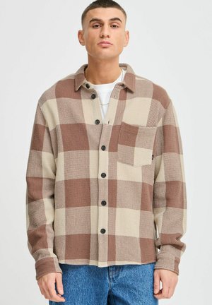 Camicia a quadri marrone e beige con taschino, realizzata in tessuto testurizzato. Presenta bottoni neri e un colletto classico.