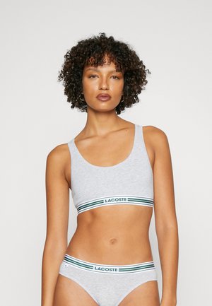 Grijze katoenen sportbeha en bijpassende slipjes met een groen-wit gestreepte elastische band met het label "LACOSTE." Gladde textuur, minimalistisch ontwerp.