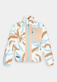 Giacca in fleece color crema con motivi astratti blu e marroni. Presenta un alto colletto, tasche con zip e pannelli beige a contrasto.