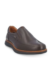 Zapato de piel marrón tipo slipper con un acabado suave, puntera redonda, paneles laterales elásticos y una suela contrastante en color beige con detalles de costura.