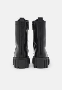 Botas de cuero negras hasta el tobillo con suela gruesa, cierre de cremallera en la parte trasera y acabado texturizado. Presenta una marca en el talón y costuras reforzadas.