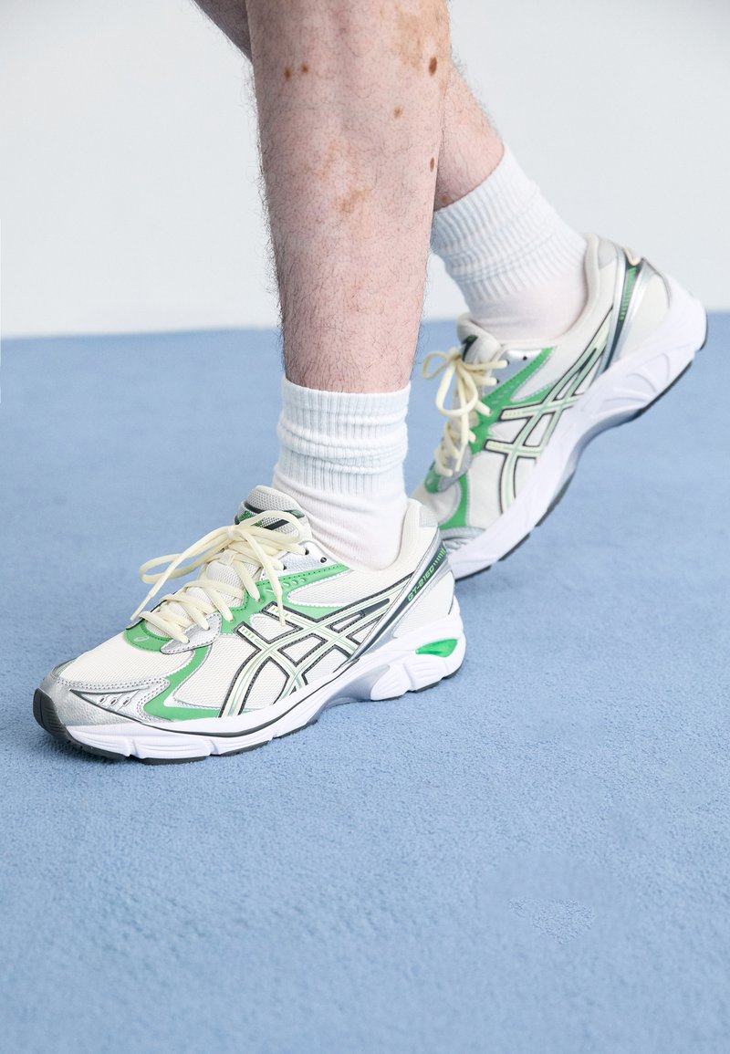 Weiße und grüne Laufschuhe bestehen aus Mesh- und Synthetikmaterialien, haben eine runde Zehenpartie und gepolsterte Sohlen, die mit silbernen Akzenten versehen sind.