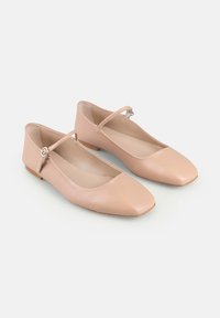 O pereche de balerini bej din piele, cu boturi pătrate și curele subțiri cu cataramă, așezați pe un fundal alb.