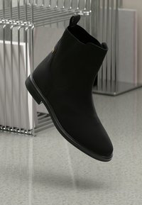 Stivali neri alla caviglia in materiale liscio, con dettagli laterali a coste e design senza chiusura. Presentano un tacco basso e un piccolo logo dorato.