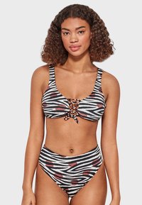 Bikini de rayas blancas y negras con puntos rojos, que presenta un detalle de cordones en la parte superior y una parte inferior de cintura alta. Textura suave.