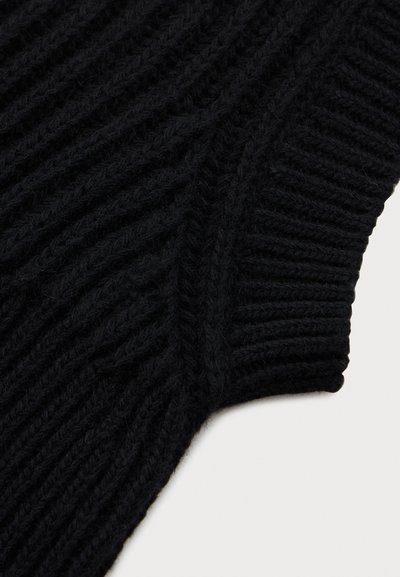 Detalhe de tecido de malha canelada preta com padrões diagonais e verticais, mostrando a textura e um punho de manga sobre um fundo claro.