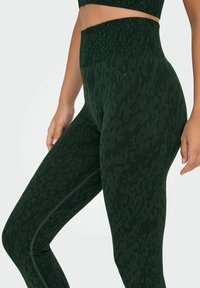 Leggings verde scuro con un sottile motivo leopardato, vita alta, tessuto testurizzato e dettagli sulle cuciture laterali.