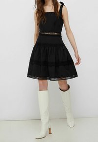 Vestito nero con un corpetto aderente, spalline a fiocco e una gonna svasata con bordo in pizzo. Abbinato a stivali alti in pelle bianca.