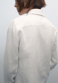 Wit linnen overhemd met een kraag en lange mouwen, met een gladde textuur en een minimalistisch ontwerp. Achteraanzicht getoond.