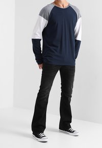 Mörkblå långärmad skjorta med grå och vita raglanärmar, matchad med svarta jeans och svarta sneakers. Avslappnad passform och bekvämt tyg.